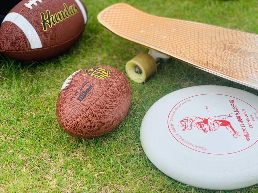 A close-up of sports equipment including a football, skateboard, and frisbee on grass.