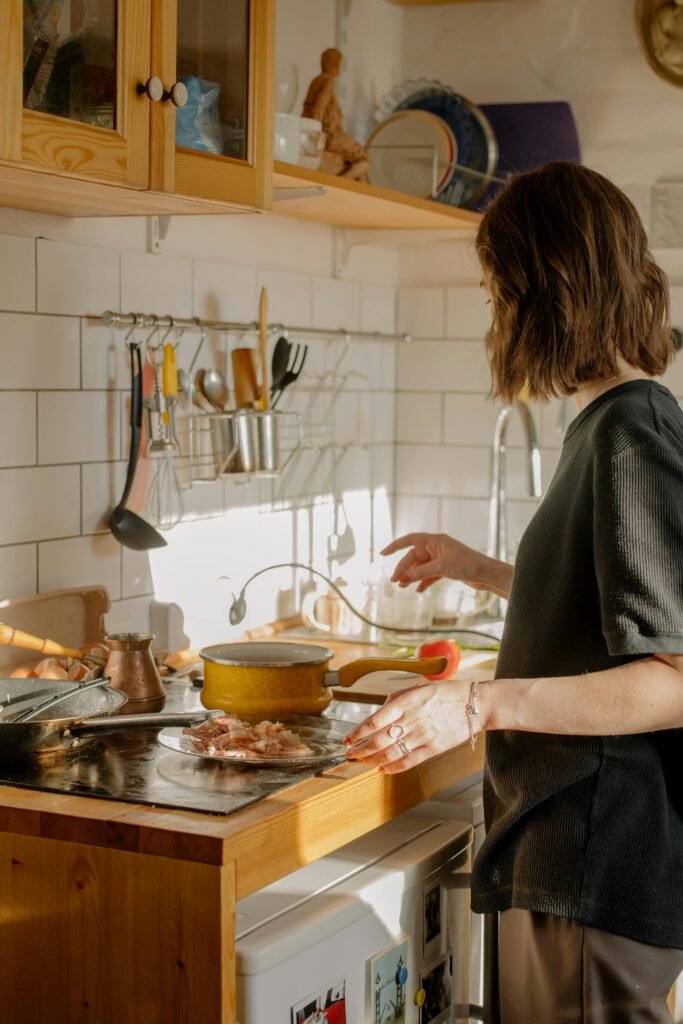 A woman cooks breakfast in a sunlit kitchen, featuring bacon and kitchenware.